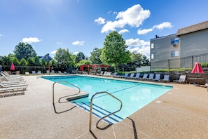 A swimming pool with lounge chairs and umbrellas, surrounded by trees and a building. - Walk to Weirs Beach! Family Escape w/ Balcony (Laconia)