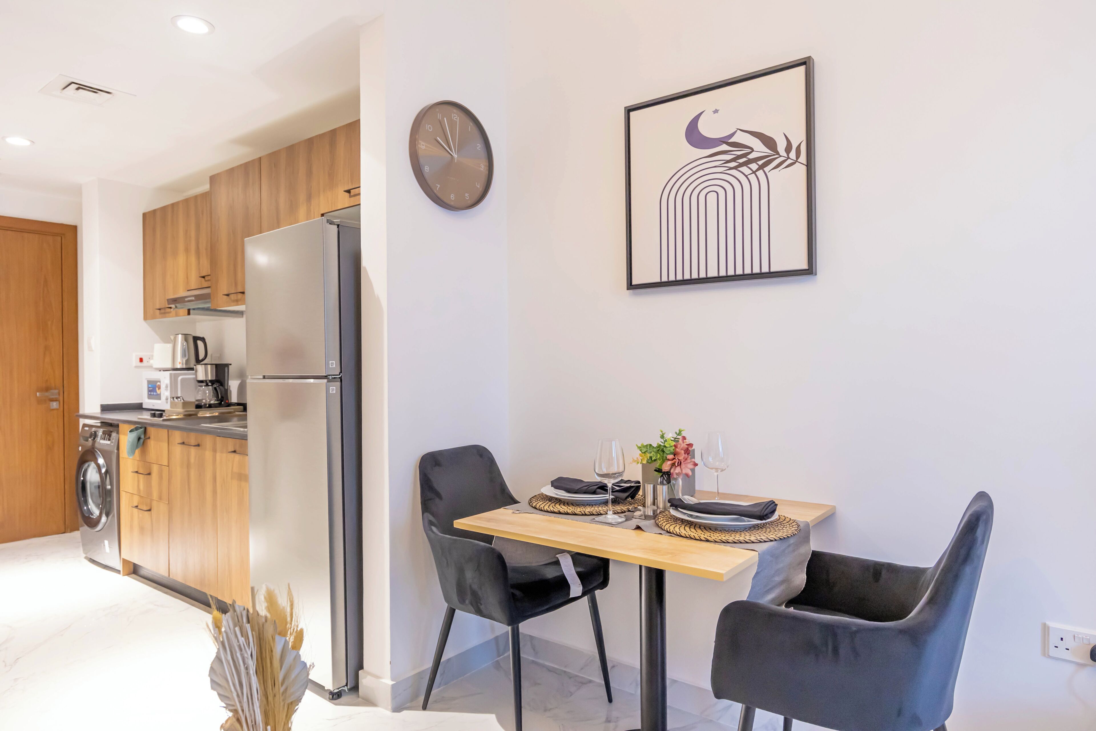 A modern kitchen with a built-in refrigerator, wooden cabinets, and a dining area with two chairs and a table set for two.