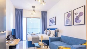 Una habitación de hotel moderna con una cama, un sofá azul, un escritorio con una computadora portátil, una zona de comedor y obras de arte en las paredes.
