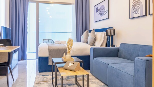 Habitación de hotel moderna con cama, sofá azul, escritorio y vistas al exterior.