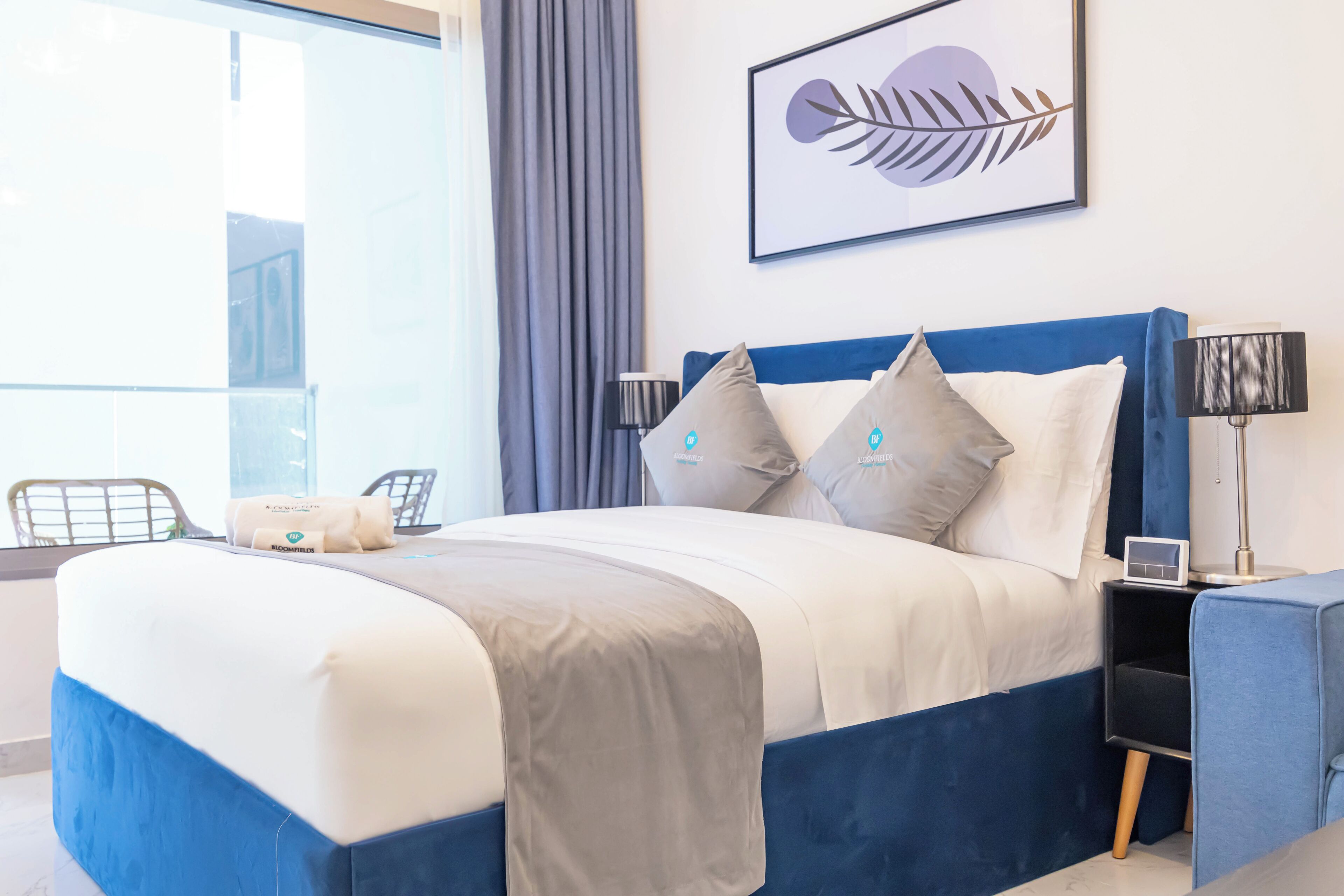 A modern hotel room with a bed, a nightstand, a lamp, a chair, and a window with curtains.
