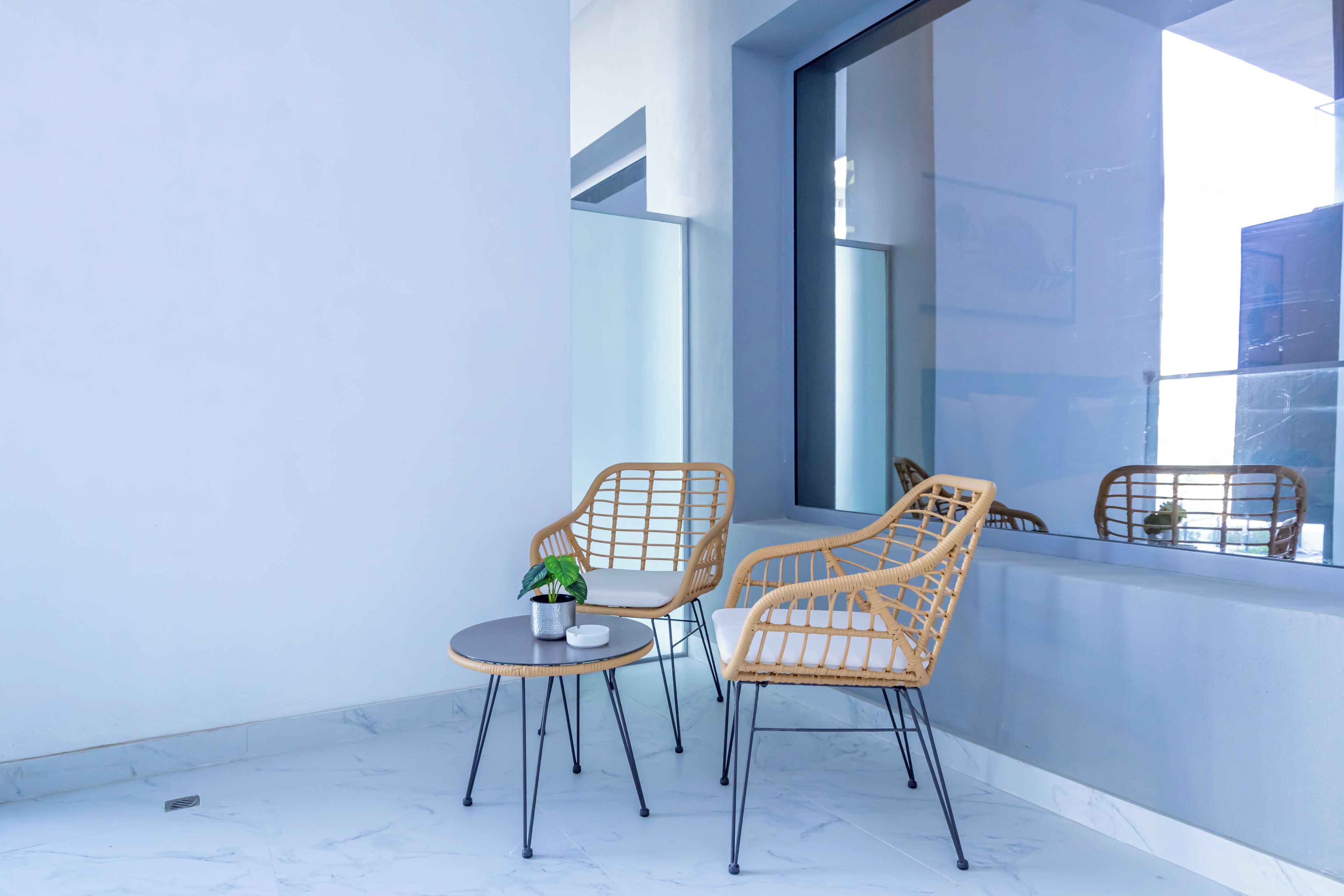 A balcony with two wicker chairs, a small table, and a potted plant.