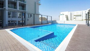 Una piscina en la azotea con borde de azulejos, rodeada de edificios modernos con balcones.