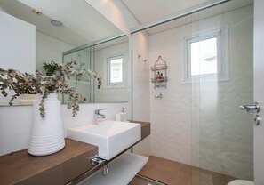 A modern bathroom with a white sink, a mirror, a shower, and a vase with dried flowers. - Corporate Stays Aqua (Altos)