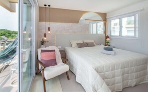 A bedroom with a large bed, a chair, a bedside table, and a view of the outdoors. - Corporate Stays Aqua (Altos)