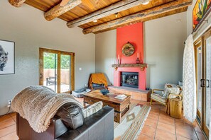 A living room with a fireplace, wooden ceiling beams, and a sofa with a throw blanket. - Adobe-Style Taos Home with Great Views! (Taos)