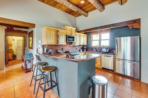 A kitchen with a central island, wooden cabinets, stainless steel appliances, and a stone backsplash. - Adobe-Style Taos Home with Great Views! (Taos)