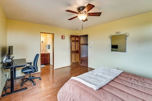 Ein Schlafzimmer mit Bett, Schreibtisch mit Stuhl, Deckenventilator und Spiegel an der Wand.