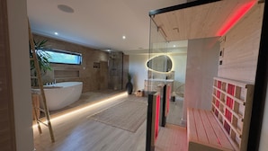 A modern bathroom with a large bathtub, glass shower enclosure, and a wooden floor.