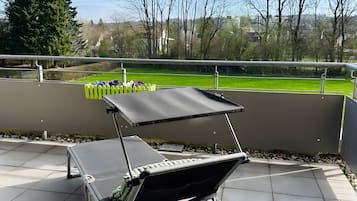 Eine Terrasse mit Klapptisch und -stühlen, Blick auf einen Park mit Bäumen und einer Rasenfläche.