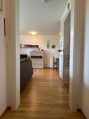 Ein schmaler Flur, der in einen Wohnbereich mit einem Sofa, einem Holzschrank und einer Glastür führt.