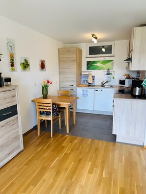 Eine moderne Küche mit Holzschränken, einem Esstisch mit Stühlen, einer Kaffeemaschine und einer Mikrowelle.
