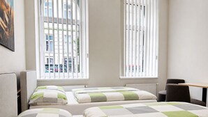 Habitación de hotel con dos camas, un escritorio y ventanas amplias con persianas.