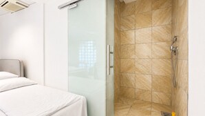 Un baño moderno con cabina de ducha de vidrio, inodoro y cama con ropa de cama blanca.