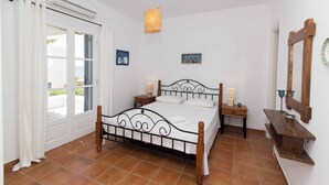 A bedroom with a bed, bedside tables, a hanging light, a window with curtains, and a wall-mounted mirror. - Picturesque home with amazing view (Paros)