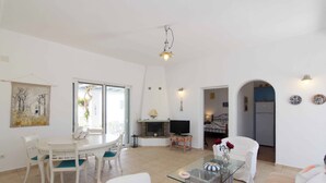 A spacious living area with a dining table, chairs, a glass coffee table, a sofa, a TV, and a fireplace. - Picturesque home with amazing view (Paros)
