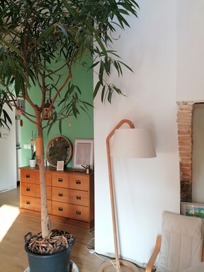 A room with a potted tree, a wooden dresser, a floor lamp, and a brick wall. - Family home on the edge of the forest (Salles)