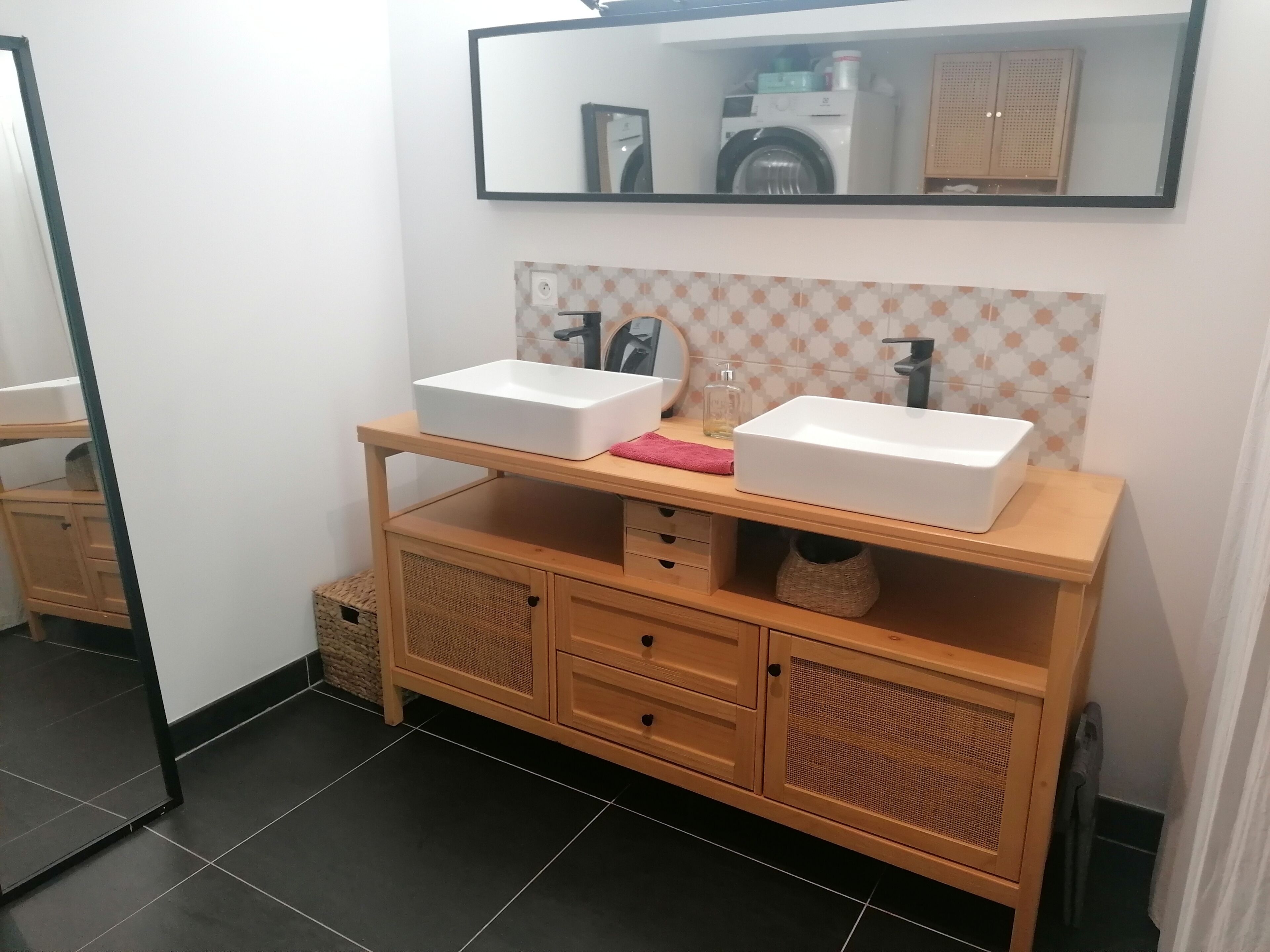 Une salle de bain avec un meuble-lavabo en bois, deux vasques, un miroir et un pare-feu en carreaux.