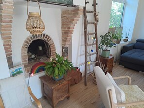 Ein gemütliches Wohnzimmer mit Kamin aus Ziegeln, einer Holzleiter, einer Topfpflanze und einem blauen Sofa.