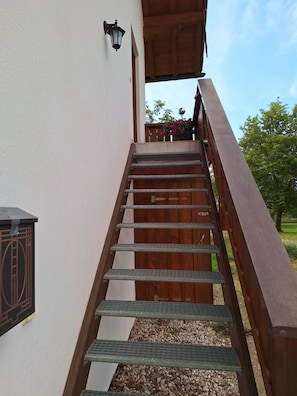 Eine Holztreppe mit Metallgeländern, die zu einem überdachten Außenbereich führt.