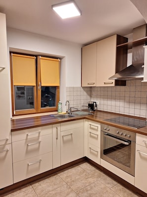 Eine Küche mit eingebautem Backofen, Spüle und einem Fenster mit gelben Rollos.
