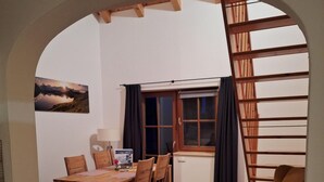 Ein Essbereich mit Holztisch und Stühlen, einem Fenster mit Vorhängen und Blick auf eine Berglandschaft.