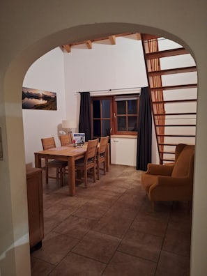 Ein Essbereich mit Holztisch und Stühlen, einem Fenster mit Vorhängen und Blick auf eine Berglandschaft.