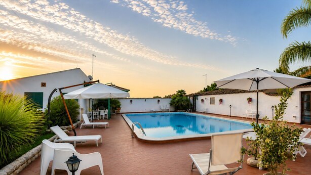A rooftop pool area with lounge chairs, umbrellas, and a clear view of the sunset. - Villa Cigno Reale by Geco Vacation Rentals (Chiaramonte Gulfi)