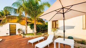 A patio with white lounge chairs, a large umbrella, and a stone wall with greenery. - Villa Cigno Reale by Geco Vacation Rentals (Chiaramonte Gulfi)