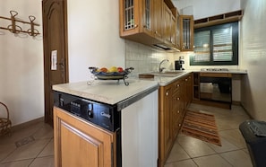 A kitchen with wooden cabinets, a built-in dishwasher, a sink, and a window with blinds. - Il Cigno Reale Green (Chiaramonte Gulfi)
