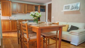 A dining area with a wooden table and chairs, a white sofa, wooden cabinets, and a kitchen in the background. - Grandparents' Cottage, 15 min from Lake Garda, View of Monte Baldo, Free Parking (San Zeno)