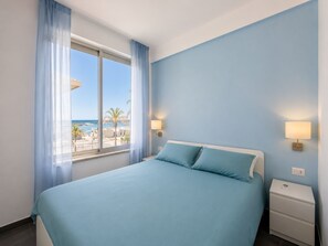 A hotel room with a bed, a nightstand, a lamp, and a view of the beach. - La Casa di Luigi by Geco Vacation Rentals (Marina Di Ragusa)