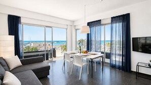 Uma sala de estar moderna com área de jantar, janelas grandes com cortinas, um sofá e uma televisão de tela plana.