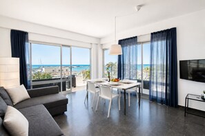 A modern living room with a dining area, large windows with curtains, a sofa, and a flat-screen TV. - La Casa di Luigi by Geco Vacation Rentals (Marina Di Ragusa)