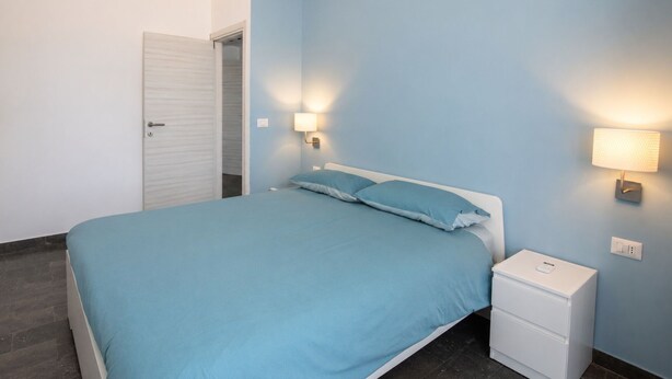 Quarto com cama, mesas de cabeceira e luminárias na parede.