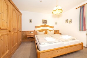 A bedroom with a wooden bed, bedside tables, a wardrobe, and a hanging light fixture. - Schneehase Vacation Rental, 40 square meters (Reit im Winkl)