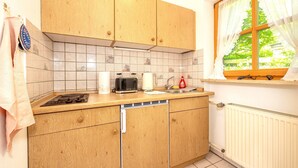 A kitchen with wooden cabinets, a toaster, a kettle, and a window with curtains. - "Schneehase" Vacation Rental with Terrace and Mountain View, 50 square meters (Reit im Winkl)