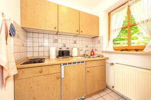 A kitchen with wooden cabinets, a toaster, a kettle, and a window with curtains. - Schneehase Vacation Rental, 40 square meters (Reit im Winkl)