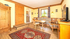 A cozy room with a wooden cabinet, a dining table with chairs, a sofa, a TV, and a window with curtains. - "Schneehase" Vacation Rental with Terrace and Mountain View, 50 square meters (Reit im Winkl)