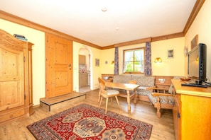 A cozy room with a wooden cabinet, a dining table with chairs, a sofa, a TV, and a window with curtains. - Bergpieper Apartment: Apartment with a View and a Balcony (Reit im Winkl)