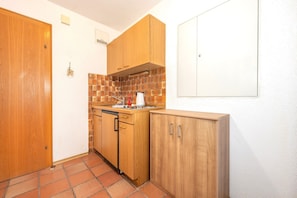 A compact kitchen with wooden cabinets, a tiled backsplash, and a white wall. - Bergpieper Apartment: Apartment with a View and a Balcony (Reit im Winkl)