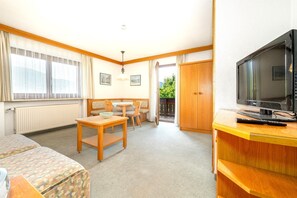 A room with a bed, a TV, a wooden table, a chair, and a window with curtains. - Bergpieper Apartment: Apartment with a View and a Balcony (Reit im Winkl)