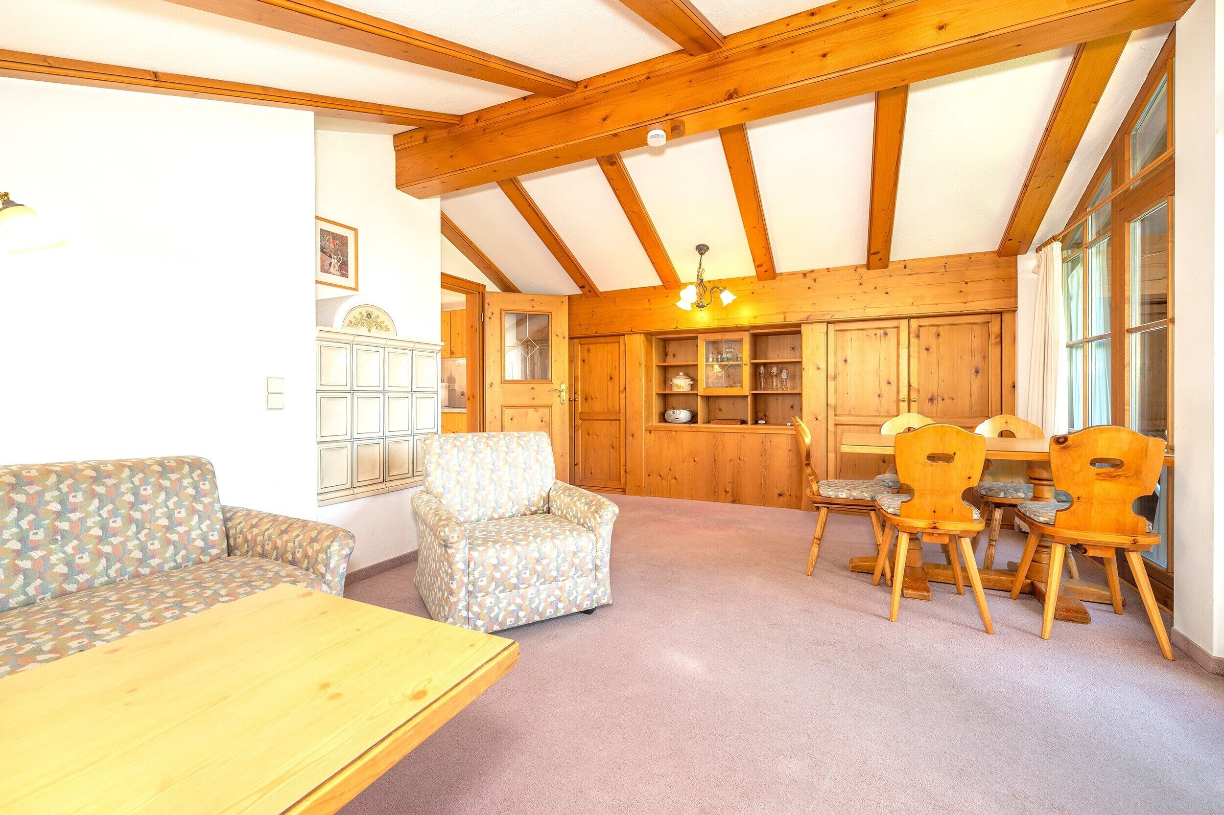 A cozy room with a wooden ceiling, a sofa, a chair, a dining table with chairs, and built-in wooden cabinets.
