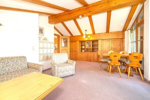 A cozy room with a wooden ceiling, a sofa, a chair, a dining table with chairs, and built-in wooden cabinets. - Alpendohle Apartment: Apartment with a View and a Balcony (Reit im Winkl)