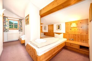 A bedroom with a wooden bed, a bedside table, a lamp, and a window with curtains. - Alpendohle Apartment: Apartment with a View and a Balcony (Reit im Winkl)
