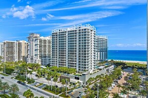 A high-rise hotel with multiple floors, a beach view, and a parking area with palm trees.
