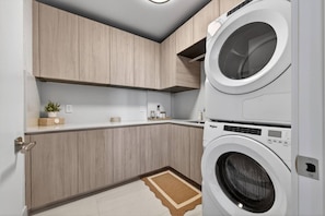 Ein Waschraum mit zwei übereinander gestapelten Frontlader-Waschmaschinen, Holzausbau, einer weißen Arbeitsplatte und einem kleinen Teppich.