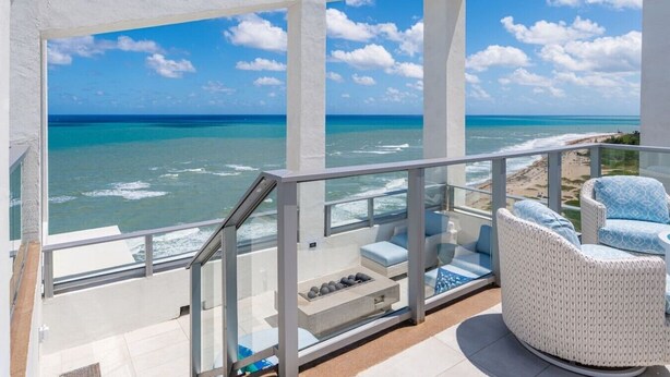 A balcony with a view of the ocean, white wicker furniture, and a glass railing.