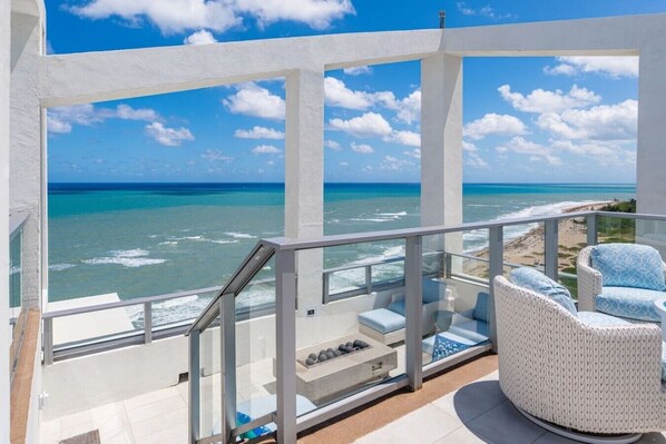 A balcony with a view of the ocean, white wicker furniture, and a glass railing.