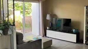 Ett modernt vardagsrum med en soffa, en tv och en skjutdörr i glas som leder ut till en balkong.
